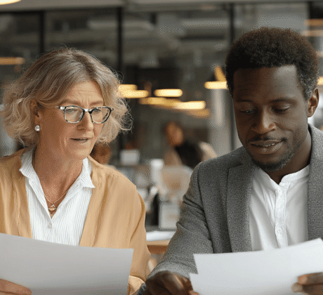 Eine ältere Frau unterhält sich mit einem Mann im Büro während Sie sich Dokumente in Ihrer Hand konzentriert anschauen.