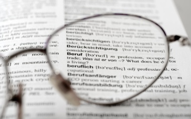 Ein offenes Wörterbuch mit dem Zoom auf eine Brillenglas.