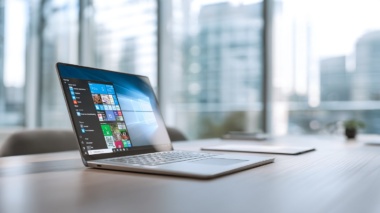 Offener Laptop auf einem modernen Büroschreibtisch, Bildschirm klar im Fokus mit sichtbaren Microsoft-Tools wie Teams, Outlook und Windows-Oberfläche,