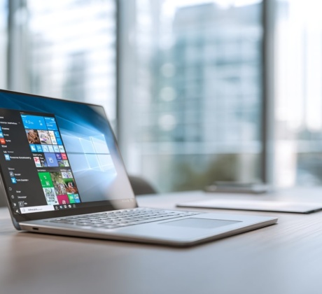 Offener Laptop auf einem modernen Büroschreibtisch, Bildschirm klar im Fokus mit sichtbaren Microsoft-Tools wie Teams, Outlook und Windows-Oberfläche,