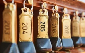 Nahaufnahme von mehreren schweren, gold-schwarzen Hotelschlüsseln, die ordentlich an Haken hängen. Die Schlüsselanhänger sind mit Zimmernummern wie 204, 205, 206 und 207 beschriftet.