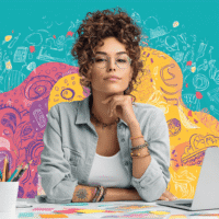 Junge, hippe Marketing-Mitarbeiterin arbeitet begeistert am Schreibtisch mit Laptop und bunten Notizen – Symbol für Kreativität und Marketing.