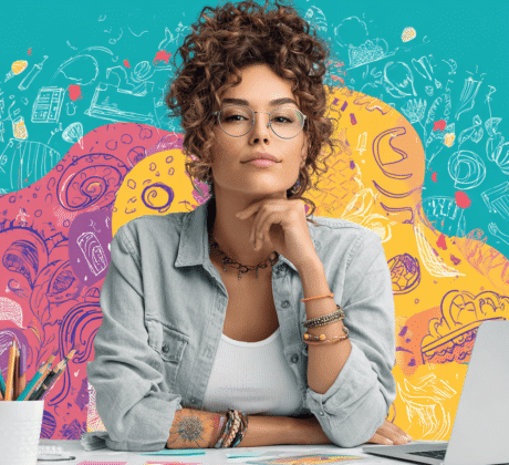 Junge, hippe Marketing-Mitarbeiterin arbeitet begeistert am Schreibtisch mit Laptop und bunten Notizen – Symbol für Kreativität und Marketing.