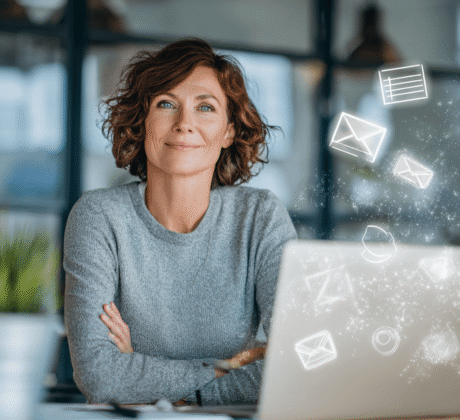 Frau Ende 40 arbeitet im modernen Büro am Laptop, über dem ein Hologramm mit E-Mail- und Kalendersymbolen schwebt – Symbol für Outlook, E-Mail und Kalender.