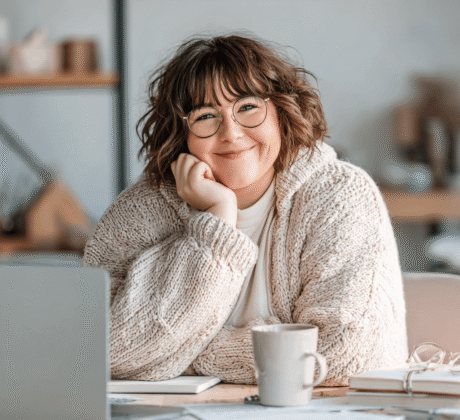 Plus-Size Frau mit Brille am Schreibtisch bei einer Online-Weiterbildung für Sekretärinnen, lächelnd und motiviert beim Lernen.