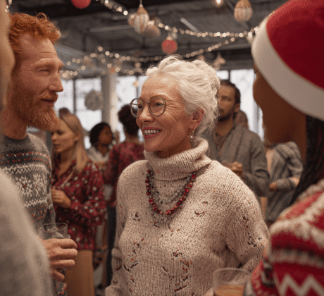 Kolleg:innen unterschiedlicher Altersgruppen lachen und feiern in einem modern dekorierten Büro mit Lichterketten – Weihnachtsfeier im Büro, fröhliche Teamstimmung.