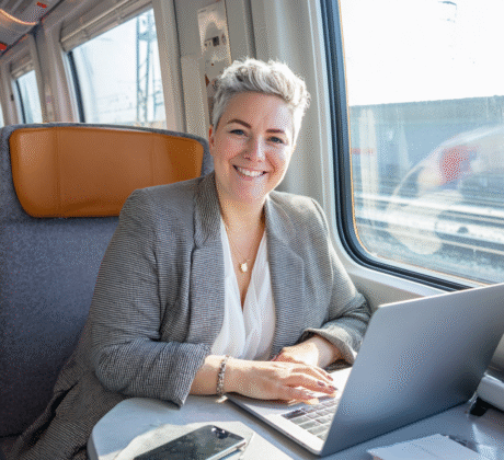 Mehrgewichtige Frau im Blazer arbeitet im Zug an Laptop und Smartphone – Symbol für Geschäftsreise und mobiles Arbeiten.