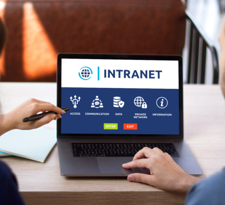 Zwei Kolleg:innen sitzen am Schreibtisch und schauen gemeinsam auf einen Laptop, auf dem Intranet steht.