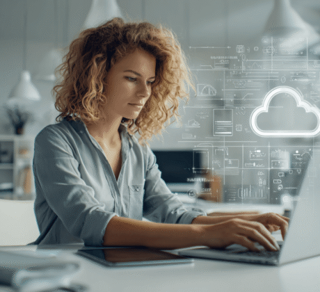 Junge Büromitarbeiterin mit dunkelblonden Locken am Laptop, über ihr ein Wolken-Hologram. Symbolbild für papierloses Büro