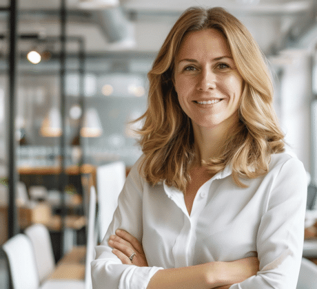 Feelgood Managerin strahlt in die Kamera, im Hintergrund ist ein modernes helles Büro zu sehen.