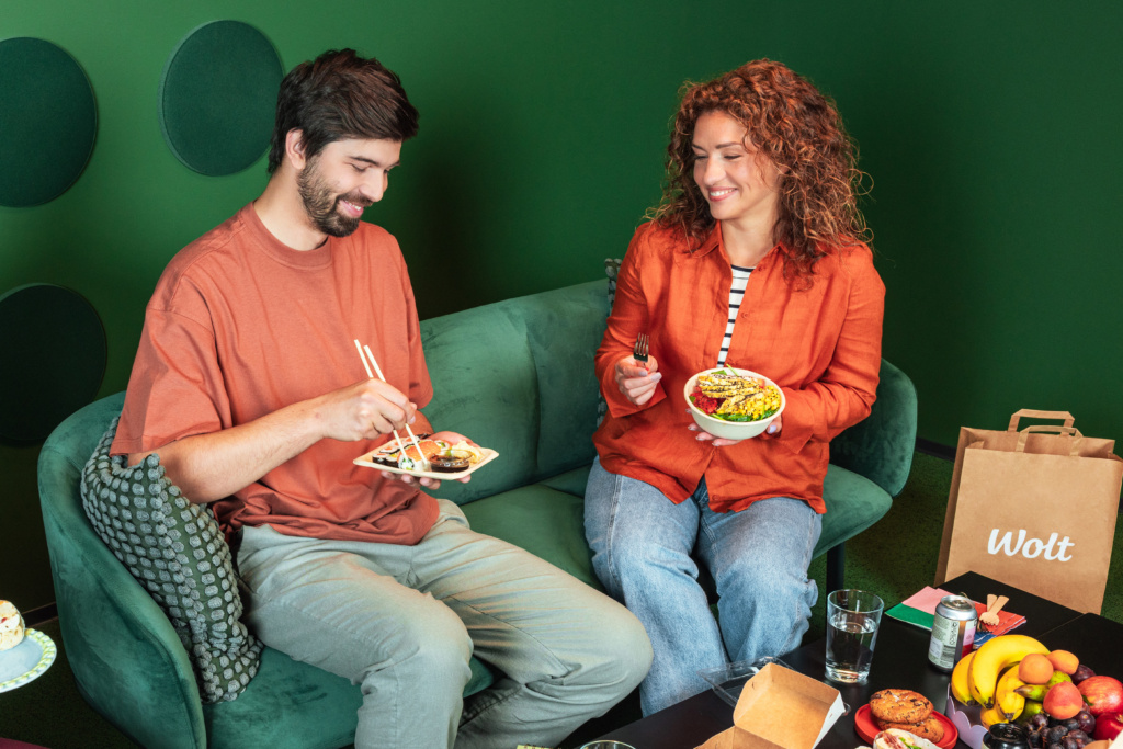 Zwei Mitarbeitende sitzen auf einem Sofa beim Mittagessen.