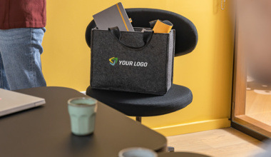 Eine graue Desk Sharing Bag mit Tragegriffen und einem Platzhalter-Logo („YOUR LOGO“) steht auf einem schwarzen Bürostuhl.